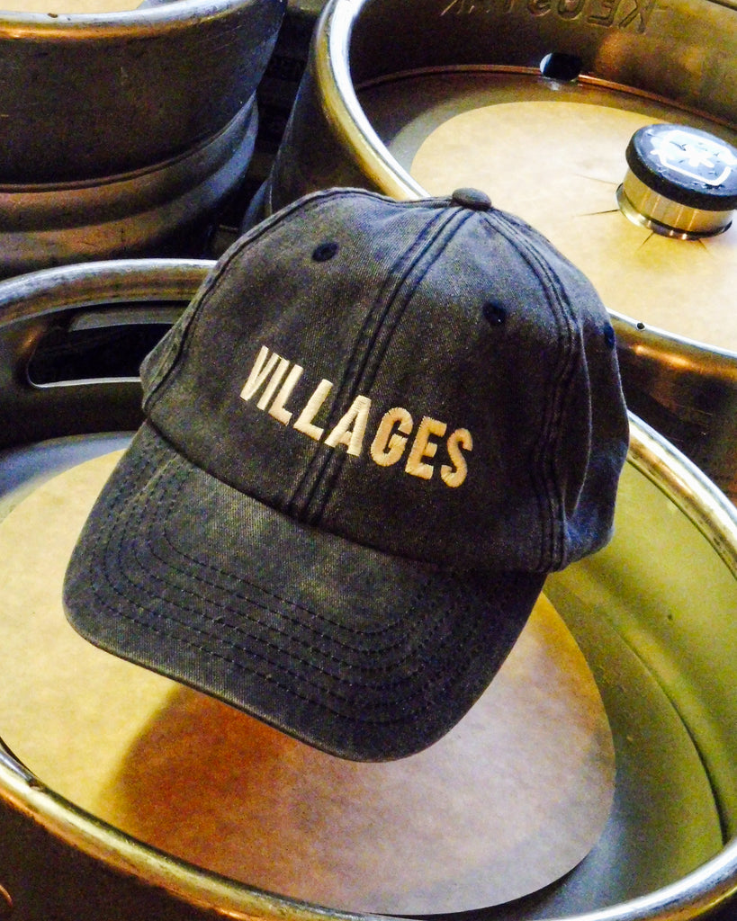Black cap with 'VILLAGES' text on top of metal beer kegs